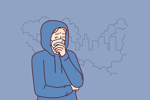 Man suffers from harmful emissions from industrial factory and wears mouth mask to protect against toxic smoke. Guy is experiencing health problems due to toxic emissions from polluting factory