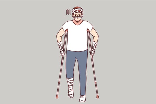 Ill man with bandages on hands and head uses walking aids after being involved in car accident. Guy injured in car accident needs long-term treatment and rehabilitation to restore health