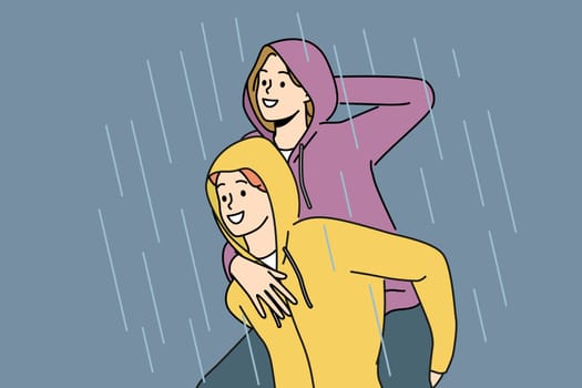 Happy couple walks in rain enjoying downpour after long drought and not wanting to go home. Man in waterproof hood rolls laughing girlfriend on back and enjoys autumn weather with rain