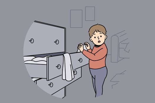 Little boy is standing near closet with clothes, looking at textiles with curiosity and studying world around. Childish pranks of funny boy throwing clothes from drawer making mess while playing