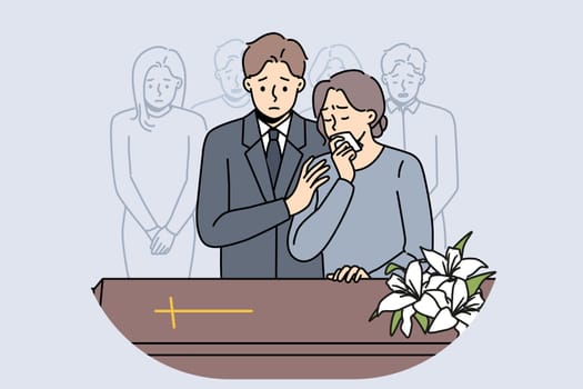 People at funeral ceremony stand near coffin with catholic cross and mourn deceased to say farewell. Upset friends and relatives at church service before funeral of man of christian faith