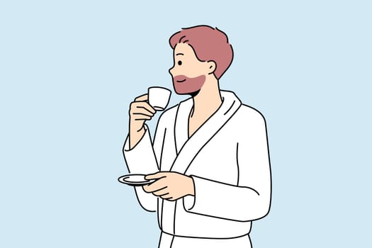 Man in bathrobe drinks coffee enjoying hot tart drink after waking up in morning. Successful young man with tea having rest in hotel or using services of spa center during vacation or weekend