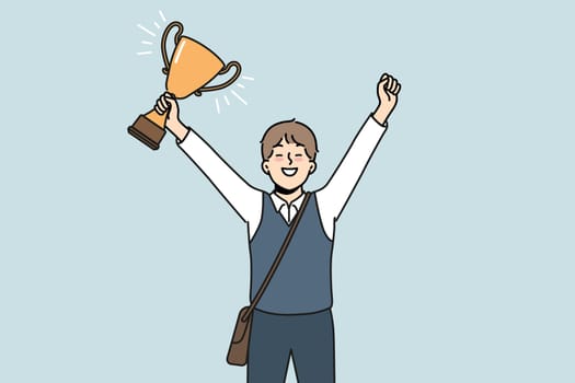 Schoolboy with golden cup rejoices at award received for winning school mathematics olympiad. Schoolboy with trophy makes winning gesture demonstrating leadership qualities while receiving education