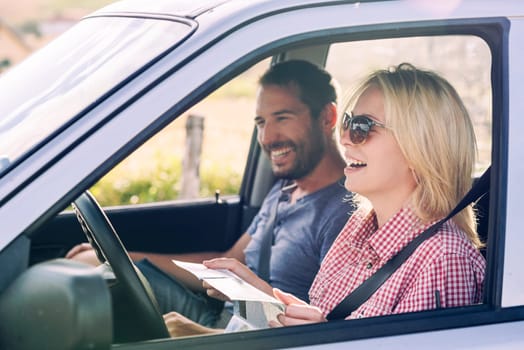 Happy couple traveling by car in nature and looking in map. Carefree friend travelers on countryside roadtrip journey. Young woman and man driving to adventure holiday.