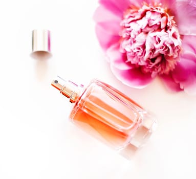 Top view of luxury perfume bottle and pink peony flower on white background. Female cosmetic and makeup accessory still life. Feminine cologne spray overhead.