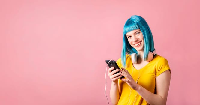 Trendy young woman with blue dyed hair holding smartphone and listen to music. Hipster girl with headphones over neon pastel background with copyspace.