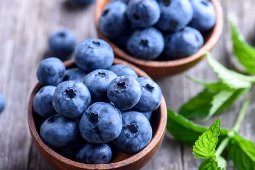 Bowl of fresh blueberries on rustic wooden table. Healthy organic seasonal fruit background. Organic food blueberries and mint leaf for healthy lifestyle. Closeup