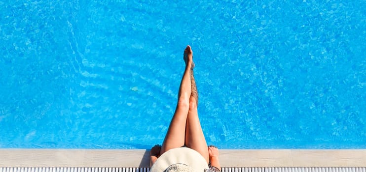 Sexy woman in bikini and sunhat relaxing in swimming pool. Top view of lady in swimsuit and hat in luxury hotel resort poolside. Summer holiday vacation lifestyle. Hot female legs in water.