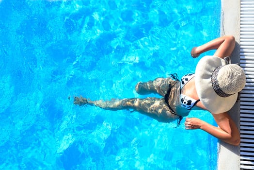Sexy woman in bikini and sunhat relaxing in swimming pool. Top view of lady in swimsuit and hat in luxury hotel resort poolside. Summer holiday vacation lifestyle.