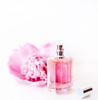 Luxury perfume bottle and pink peony flower isolated on white background. Female cosmetic and girly  makeup accessory still life. Feminine cologne spray.