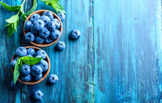 Bowl of fresh blueberries on blue rustic wooden table from above. Top view of healthy organic seasonal fruit pattern background. Organic food blueberries and mint leaf overhead for healthy lifestyle.