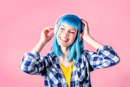 Trendy young woman with blue dyed listen to music and dancing. Hipster girl with headphones over neon pastel background.