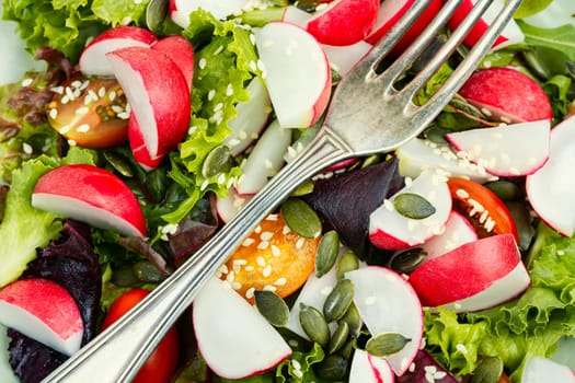 Portion of vegetable salad with radish, greens, tomato and sesame on a gray background.