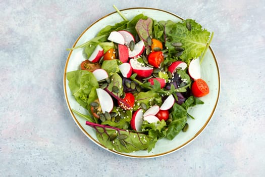 Portion of vegetable salad with radish, greens, tomato and sesame on a gray background.