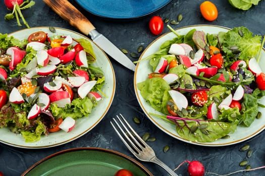 Portion of vegetable salad with radish, greens, tomato and sesame on a gray background.