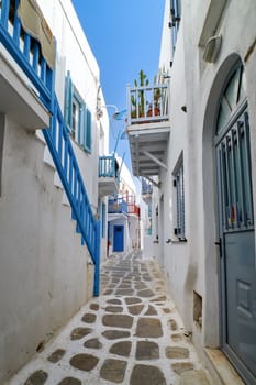 Charming traditional narrow streets and beautiful alleyways of Greek island towns. Whitewashed houses, flower pots, blue, grey and red balconies, stairs and doors, cobble paved street. Summer day sunshine. Mykonos, Greece