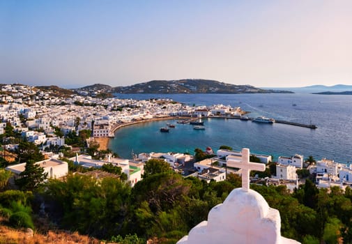 Beautiful sunset view, Chora, main town of Mykonos, Cyclades, Greece from roof top of a Greek Orthodox church. Golden hour, harbor, ships, cruises, whitewashed houses and distant islands in hazy background. Vacations, leisure, Mediterranean lifestyle