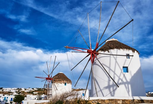 Famous tourist attraction of Mykonos, Cyclades, Greece. Two traditional whitewashed windmills by waterfront and Chora town. Summer evening, blue sky, beautiful clouds. Travel destination, iconic view. Diagonal composition.