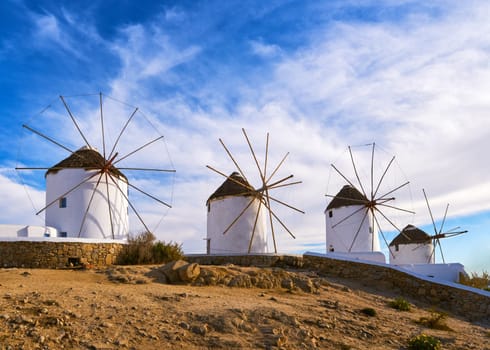 Famous tourist attraction of Mykonos, Cyclades, Greece. Four traditional whitewashed windmills by waterfront of Chora harbor. Summer evening, blue sky, beautiful clouds. Travel destination, iconic view.