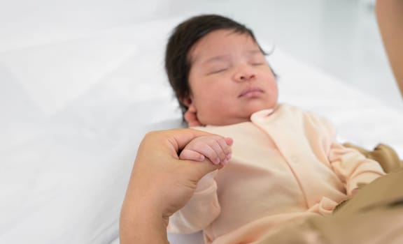 Hand of mother holding finger of newborn hand. Adorable infant girl 1 month sleeping on mom arm at home. Care, love and mothers day concept.