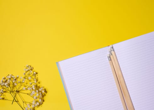 Open notebook, wooden pencil on yellow background, top view