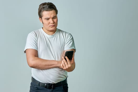 A man looks at the phone screen on a gray background. High quality photo