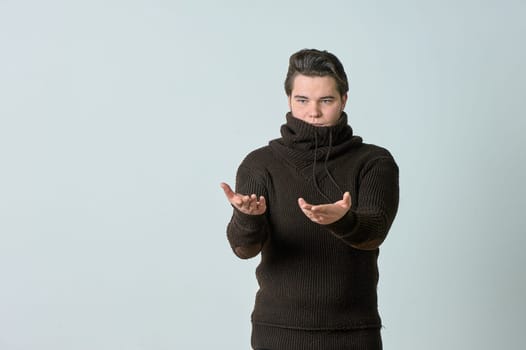 A man on a gray background in a brown sweater showing emotions, shows his hands. High quality photo