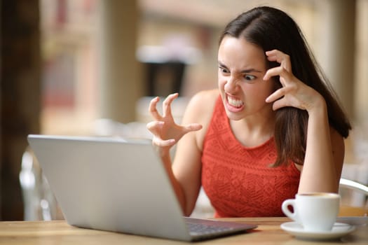 Angry woman having problems with a laptop in a bar terrace