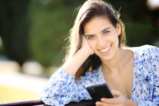Beautiful happy woman posing looking at camera holding phone in a park