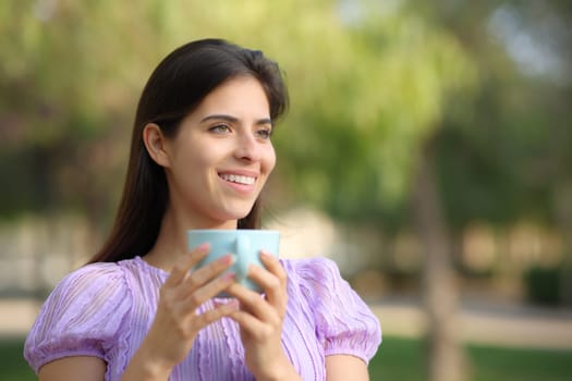 Happy female holding coffee cup standing in a green park
