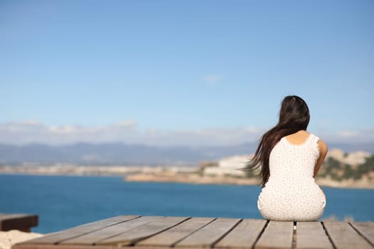 Back view portrait of a woman sitting contemplating ocean in the coast