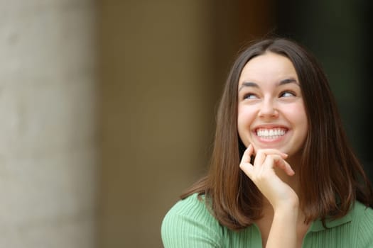 Front view of a happy woman looking at side wondering in the street