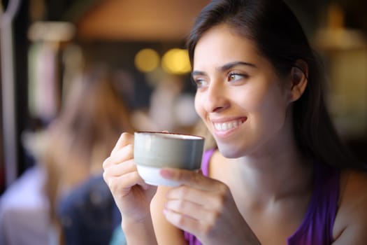 Happy woman holding coffee mug looks at side in a restaurant