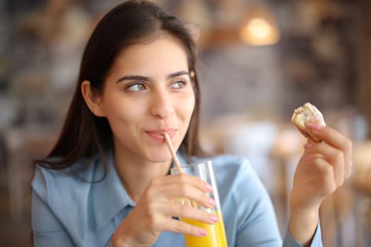 Happy woman drinking juice eating croissant in a restaurant
