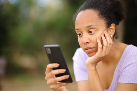 Serious black woman using cell phone sitting in a park