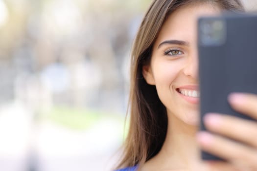 Close up front view portrait of a happy woman using cell phone with copy space looking at you