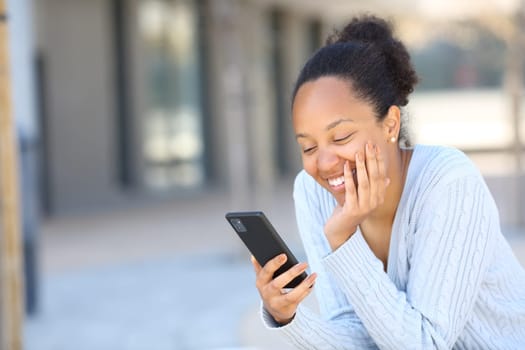 Happy black woman laughing using phone in the street