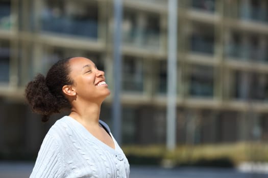 Happy black woman breathing fresh air in the street