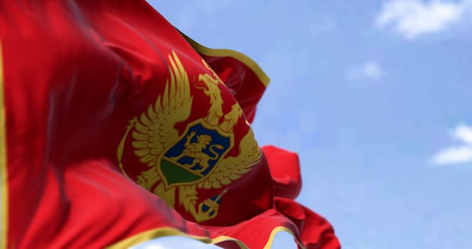 National flag of Montenegro waving in the wind on a clear day. Red with a gold border and has the coat of arms in its center. 3d illustration render, fluttering fabric. Selective focus