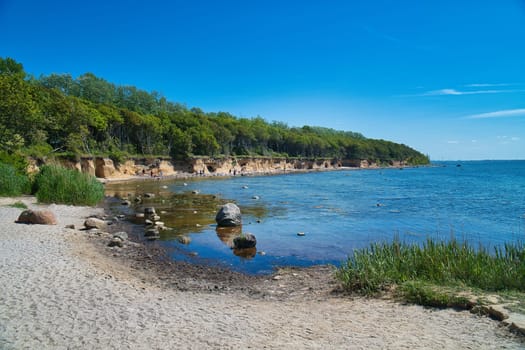 Bay on the island of Poel on the Baltic Sea. Stone beach, with trees on the coast. Sunshine on the sea.