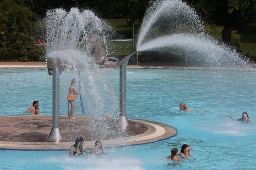 Theme picture summer -   The dog days are here - people crave to cool off at temperatures above 30 degrees Celsius,like here in the lido of Freiburg im Breisgau. Under the water fountain,young and old have fun