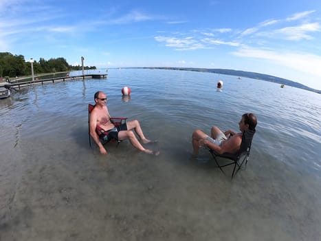 Theme picture Summer - Summer day at Lake Constance  This is how it can be endured: Despite the summer heat,these two men have positioned their sitting chair right in Lake Constance and thus find the right cooling not only for their feet.  Young and old sought to cool off on a boat trip,an excursion with the Stand Up Paddle (SUP) or while swimming. The next few days are expected to remain hot in summer if thunderstorms are likely to occur