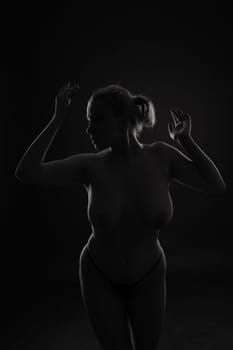 Beautiful female body. Isolated on a dark studio background. Plump woman covering breast.