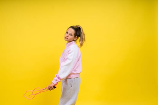 Beautiful sportsgirl with skipping rope isolated on a yellow studio