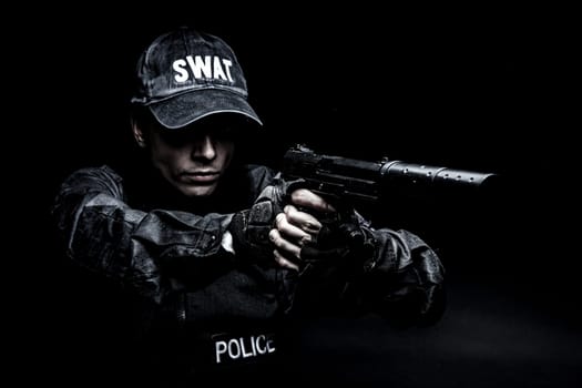 Spec ops police officer SWAT in black uniform aiming pistol with silencer, studio shot, half length