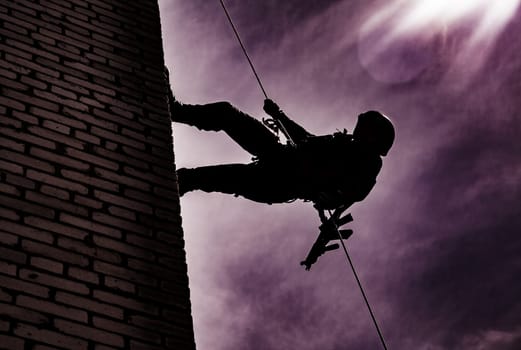 Silhouette of police officer in tactical gear descending from a height, rope exercises with weapons. Tactical rappelling, anti-terror or counter terrorism operation in darkness in rappelling harness