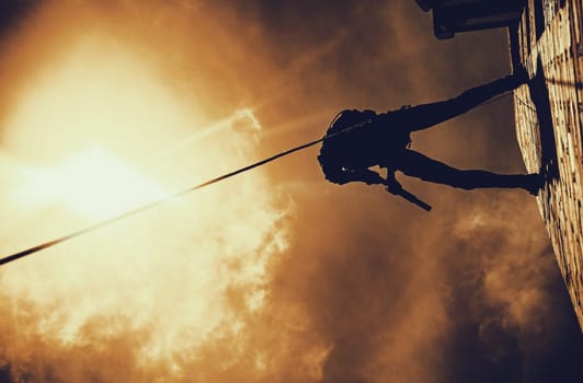 Silhouette of police officer in tactical gear descending from a height, rope exercises with weapons. Tactical rappelling, anti-terror or counter terrorism operation in darkness in rappelling harness