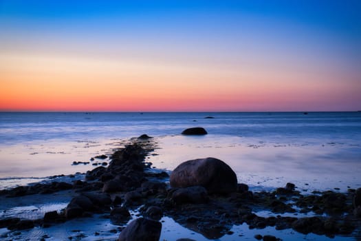 Sunset, stone beach with small and large rocks in front of the illuminated sea. Light waves. Poel island on the Baltic Sea. Nature photo from the coast