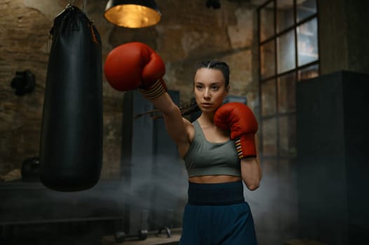 Portrait of young female boxer practicing punches wearing boxing gloves looking concentrated and confidently