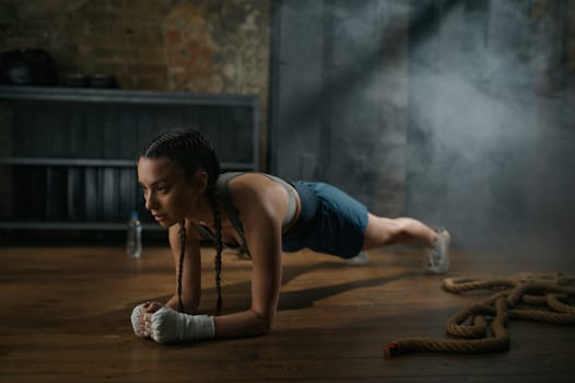 Strong woman boxer with bandaged hands standing in plank. Athletic female fighter doing intense physical training for endurance improvement